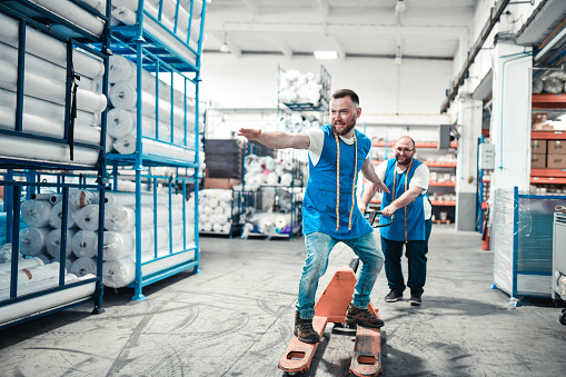 SmilingBearded Male Having Fun Riding On Manual Forklift In Warehouse