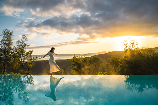 Beautiful woman walking on the edge of an infinity pool in a jungle during sunrise