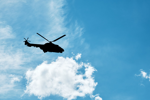 Silhouette of a helicopter flying against the blue sky background with clouds.