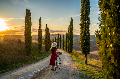 Young girl in red dress watching the sunset sitting on a vintage bicycle