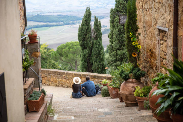 Rear view of a couple sitting on the stairs, Pienza, Italy Rear wide angle shot of a couple sitting on the stairs enjoying the view siena italy stock pictures, royalty-free photos & images