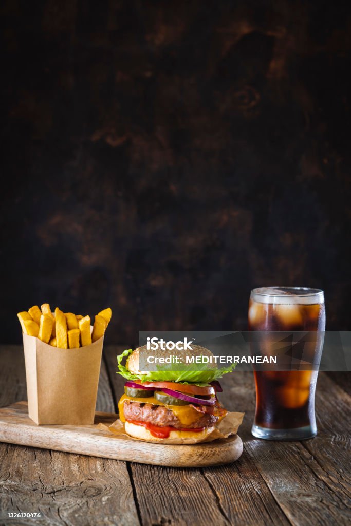 Burger combo with cola soda beverage glass and disposable french fries in kraft paper box on dark wood table Burger combo with cheeseburger hamburger cola soda beverage glass and disposable french fries in kraft paper box on dark wood table background Burger Stock Photo