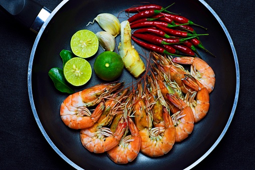 Cooked shrimps and ingredients in cooking pan - black background.