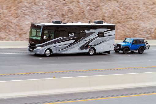 Boulder City, NV, USA – June 7, 2021: RV motorhome bus towing a jeep heading uphill on Interstate 11 in Southern Nevada near Boulder City, Nevada.