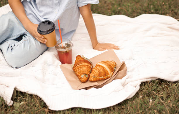 Boy kid sitting on picnic summer vacation with freshly baked croissants and glass of refreshing orange juice and cappuccino in a hand