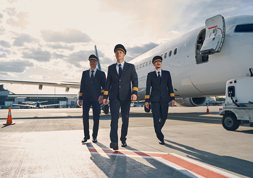 Full-length portrait of three handsome male pilots dressed in elegant uniforms walking across the runway