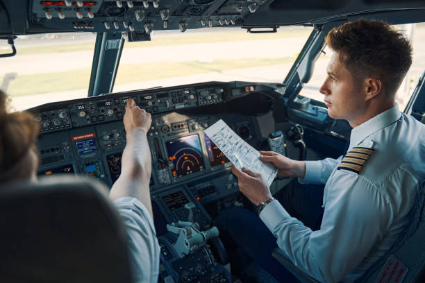 Airline captain and first officer sitting in the cockpit Co-pilot with a pre-flight checklist in his hand seated by a chief pilot in the flight deck pilot photos stock pictures, royalty-free photos & images