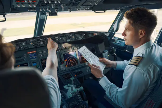 Co-pilot with a pre-flight checklist in his hand seated by a chief pilot in the flight deck