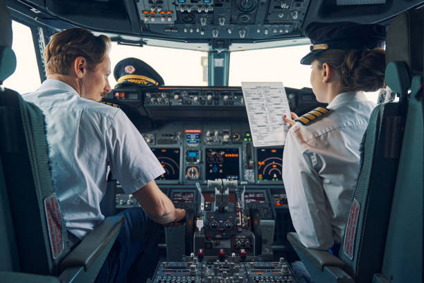 Pilot and female first officer seated in the flight deck Back view of a co-pilot with a pre-flight checklist in her hand sitting by an aircraft captain in the cockpit pilot stock pictures, royalty-free photos & images