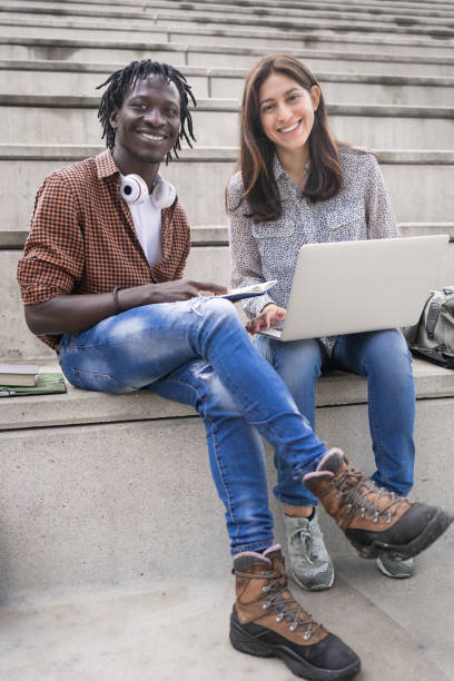 porträt von zwei lächelnden multirassischen studentenfreunden, die mit laptop an der universität arbeiten - online degree stock-fotos und bilder