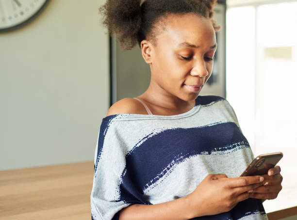 istock Young woman texting on her phone while leaning on a kitchen counter 1326138079