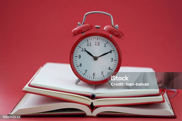 Alarm Clock Standing On Pile Of Books On Red Background Closeup Stock Photo - Download Image Now