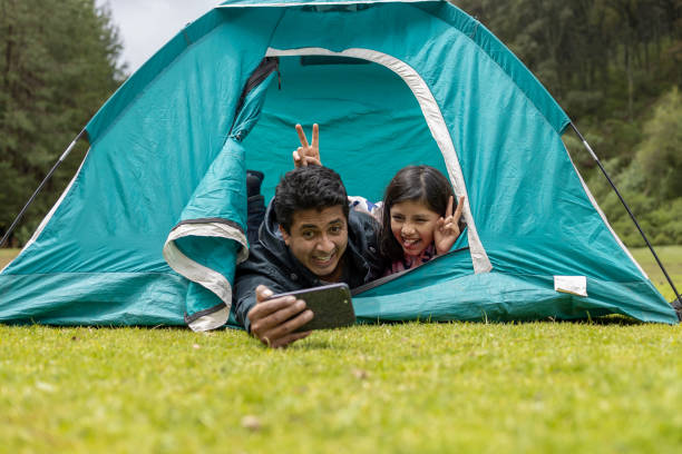 father and daughter taking selfie on camping tent