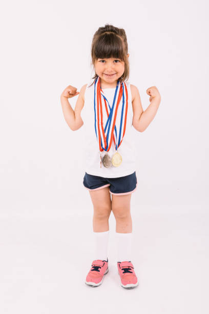 bambina con i capelli castani con medaglie campione di sport sul collo che fanno il simbolo della forza. concetto di sport e vittoria - humor athlete trophy one person foto e immagini stock