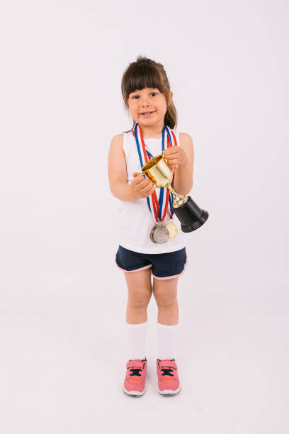 スポーツチャンピオンのメダルを持つ小さな茶色の髪の女の子は、両手でトロフィーを保持しています。スポーツと勝利のコンセプト - humor athlete trophy one person ストックフォトと画像