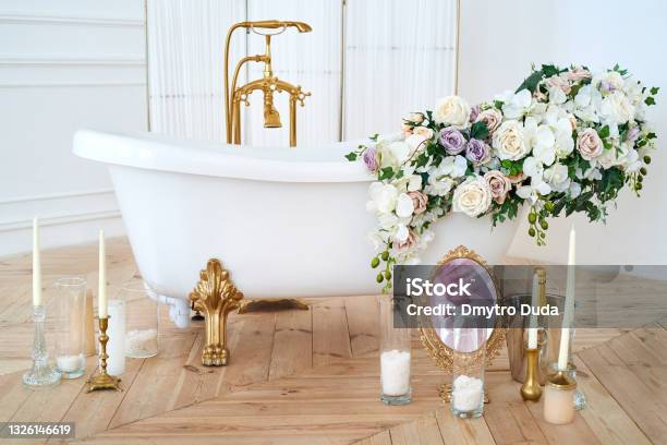 Beautiful Luxury Vintage Empty Bathtub With Lush Floral Decorations And Candles Mirror On The Floor In Bathroom Interio Copy Space Freestanding White Bath With Flowers Near Folding Screen Stock Photo - Download Image Now