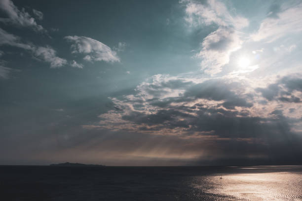 Sun rays shining though clouds over the sea in Greece. Dramatic cloudscape on mediterranean sea water surface. Color graded