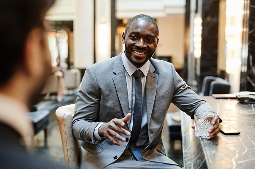 Portrait of smiling African-American businessman talking to partner at bar in hotel during business trip, copy space