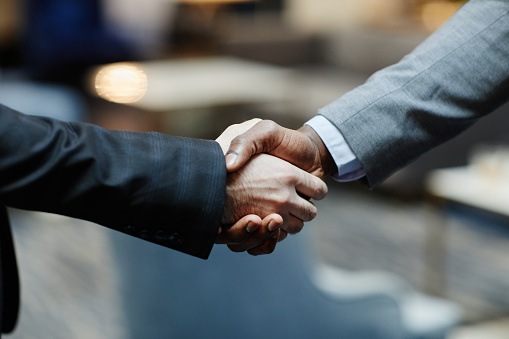 Close up of two successful businessmen shaking hands in office building lobby, copy space