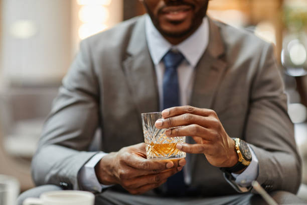 Handsome Man Holding Liquor Glass Close Up Cropped shot of successful African-American businessman enjoying glass of whiskey in hotel, copy space whiskey stock pictures, royalty-free photos & images