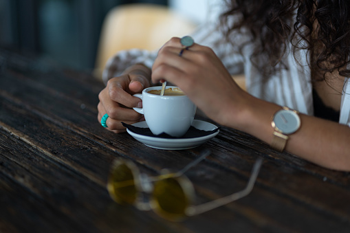 woman with rings and watch having a cup of coffee at wooden table