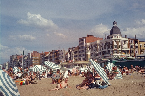 Koksijde, West Flanders, Belgium, 1964. Beach scene with vacationers on the beach at Koksijde: Also: umbrellas, buildings and deck chairs.