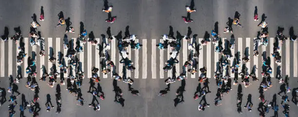Different people at a pedestrian crossing in the city - panorama shot. People at a zebra pedestrian crossing - a lot of pedestrians in an overcrowded city on a sunny day. Aerial drone banner shot.