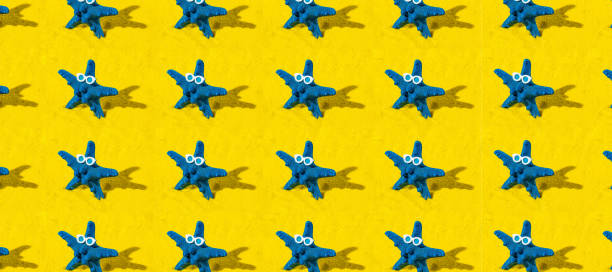 Creative pattern background with blue starfish with sunglasses on yellow sand. Minimal creative summer or vacation concept with copy space.