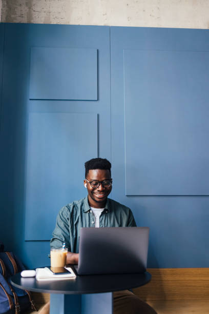 ラップトップコンピュータのコーヒーショップで働く耳にワイヤレスイヤホンを持つ幸せなビジネスマン - business blue business person businessman ストックフォトと画像