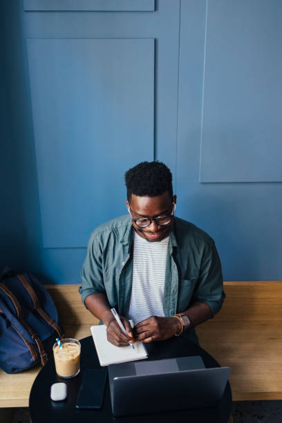 istock Happy Businessman With Wireless Earphones in Ears Writing Notes while Working in a Coffee Shop on his Laptop Computer 1326165997