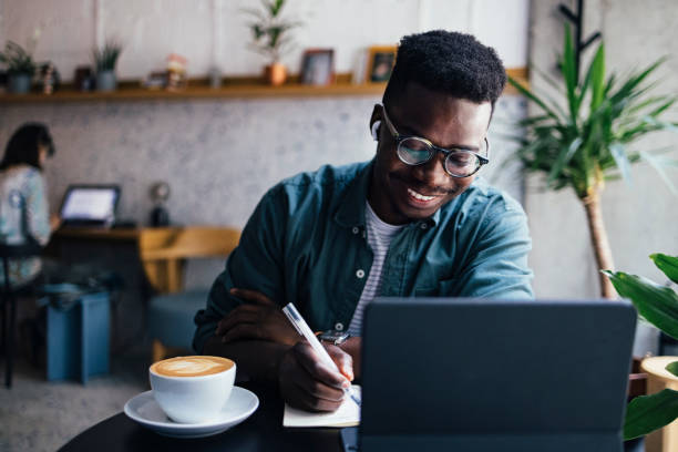istock Happy Businessman With Wireless Earphones in Ears Writing Notes while Working in a Coffee Shop on his Laptop Computer 1326166044