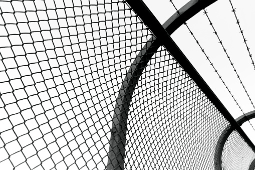 Black and white closeup mesh link fence with barbed wire, background with copy space, full frame horizontal composition