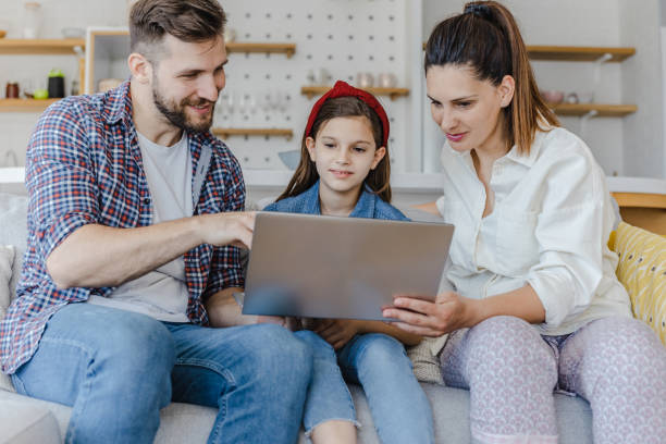 istock Smiling parents and their daughter are using laptop on sofa at home 1326169132