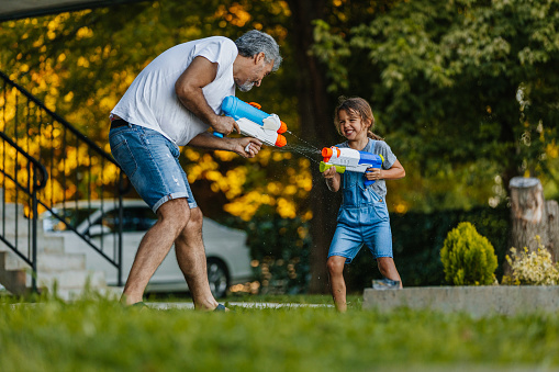 Grandfather and his grandson playing with water guns at the backyard