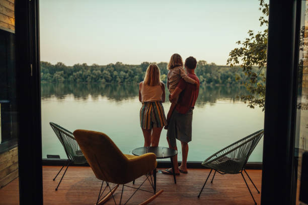Adorable family of three at the terrace looking at the river A scenic view of family from inside of weekend cottage by the riverside lake stock pictures, royalty-free photos & images