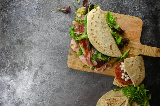 Italian street food flat lay with piadina on a wooden cutting board. Piadina romagnola - Italian flatbread