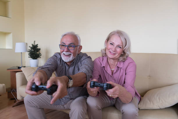 handsome senior mann und seine ältere frau spielen spielkonsole, während zeit zusammen zu hause. - gamer watching tv adult couple stock-fotos und bilder