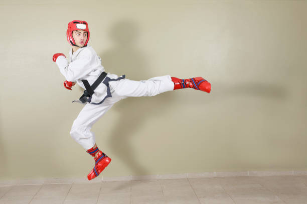 combattente taekwondo che fa un calcio posteriore volante, vestito con uniforme bianca e cintura nera. con elementi protettivi rossi. - kicking tae kwon do martial arts flying foto e immagini stock