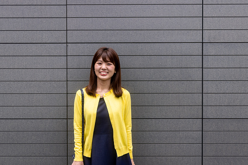 Japanese woman in yellow cardigan walking in the city for shopping and working remotely.