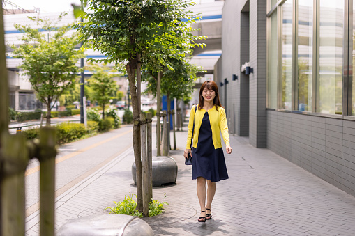 Japanese woman in yellow cardigan walking in the city for shopping and working remotely.