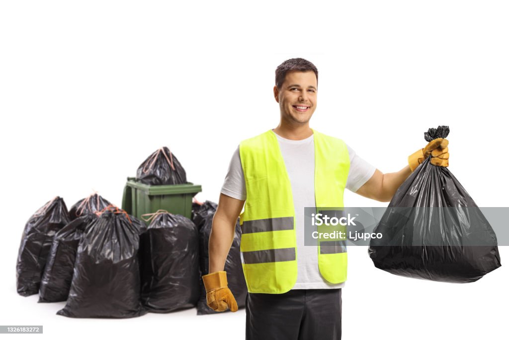 Waste collector holding a plastic bag in front of a bin and a pile of bags and smiling at camera Waste collector holding a plastic bag in front of a bin and a pile of bags and smiling at camera isolated on white background Garbage Stock Photo