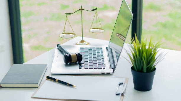 a judge's hammer rests on a laptop and gold scales with papers and pens on the lawyer's desk. - contract signing document legal system imagens e fotografias de stock