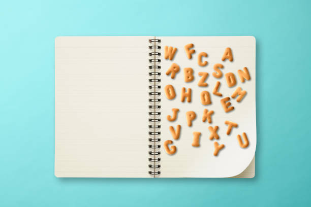 Disordered uppercase alphabet made of biscuits with spiral notebook, on light blue background with copy space.