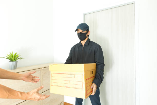Asian delivery man wearing face mask holding a cardboard boxes deliver to customer during COVID-19 outbreak. stock photo