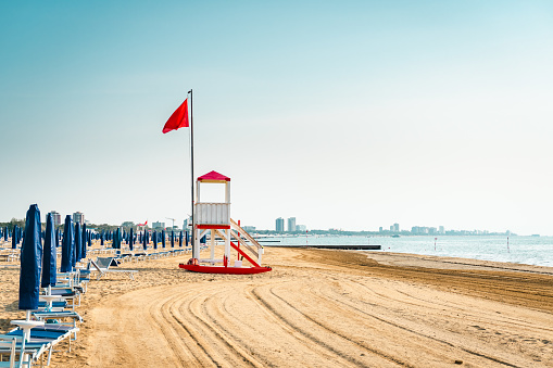Beach at the Adriatic sea coastline in Italy, Europe during summer. Traditional hut for the beach lifeguard and a red flag.