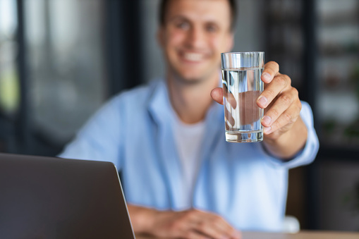 Smiling caucasian businessman or student holding glass of clean water in hand while sitting in office, copy space