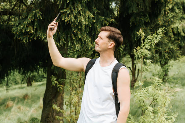 Man trying to catch signal on mobile phone outdoors in the forest. Sad traveler in hike in nature raises his hand with smartphone high up. Loss of connection, weak signal on the phone concept. hombre tratando de captar señal en el teléfono móvil al aire libre en el bosque. viajero triste en caminata en la naturaleza levanta la mano con el teléfono inteligente en lo alto. pérdida de conexión, señal débil en el concepto de teléfono.