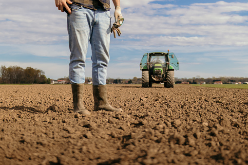 Low angle photo of a farmers feet in rubber boots with tractor in background