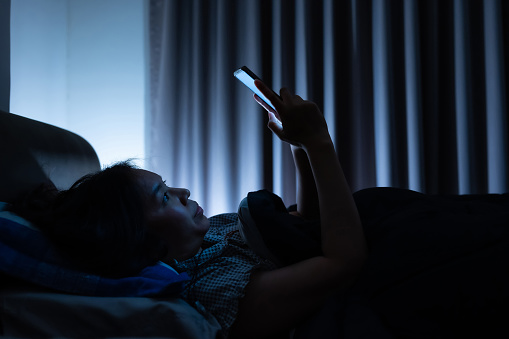 Asian woman on bed late at night and using mobile smartphone before sleep in dark bedroom