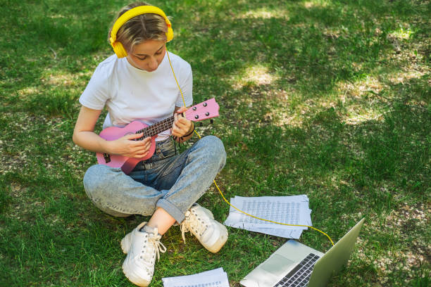 jolie adolescente jouant du ukulélé devant la caméra. cours de musique en ligne. - musical instrument nature outdoors musician photos et images de collection